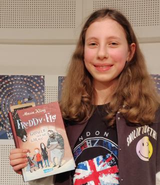 Enna Marwan aus der Karl-Foerster-Grundschule Auf dem Foto ist Enna Marwan aus der Karl-Foerster-Grundschule. Sie hält in der Hand das Buch „Freddy und Flo gruseln sich vor nix!“