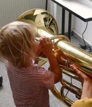 Instrumente ausprobieren ist aufregend! Ein Kind im Vorschulalter versucht, einen Ton aus einer Tuba zu bekommen!