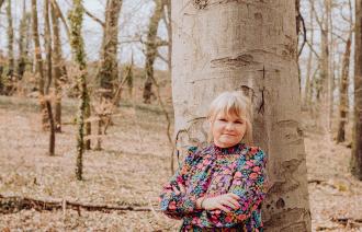 Eine Frau lehnt sich an einen Baum im Wald.