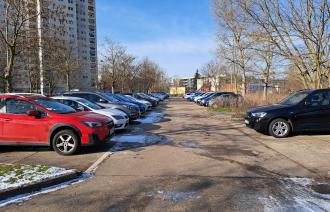 Parkplatz mit parkenden Autos und Hochhaus im Hintergrund am Falkenhorst im Schlaatz.