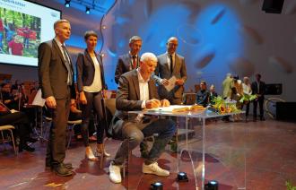 Der Geehrte Peter Schäperkötter sitzt an einem Tisch im Nikolaisaal und schreibt sich ins Goldene Buch der Stadt ein. Hinter ihm stehen Dr. Hagen Wegewitz, Mike Schubert und Sebastian Stielke.