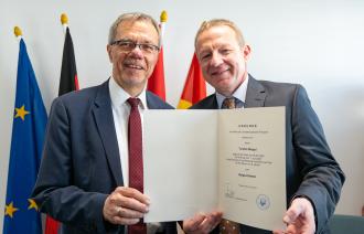 Die beiden Männer Burkhard Exner und Tobias Wiegel stehen nebeneinander und zeigen auf eine Urkunde in DIN-A4-Größe. Es ist die Ernennungsurkunde für den neuen Beigeordneten Tobias Wiegel, der für acht Jahre Beigeordneter der Stadt Potsdam sein wird.