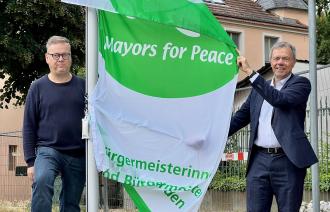 Bürgermeister Burkhard Exner und Uwe Fröhlich vom Hiroshima-Platz-Verein mit der Flagge Mayors for Peace.