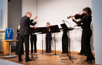 Schülerinnen der Musikschule werden dirigiert und spielen auf ihren Geigen.