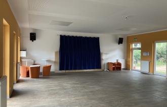 Das Foto zeigt den leeren und aufgeräumten Saal im Bürgerhaus "Kirchbergtreff" Neu Fahrland mit einigen Einrichtungsgegenständen wie Sessel und Stehtischen.