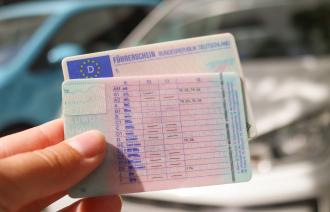 Führerscheine werden vor einem Auto in die Kamera gezeigt.