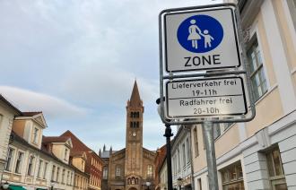 Blick in die Brandenburger Straße in Richtung St. Peter und Paul Kirche. Im Vordergrund ist das Schild "Fußgängerzone" zu sehen.