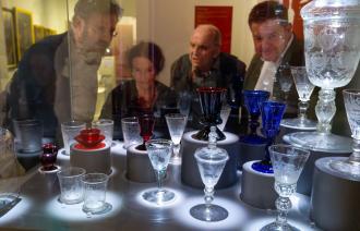 Vier Personen schauen in eine Vitrine, in der barocke Potsdamer Gläser ausgestellt werden.