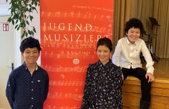 Die Drillinge Markus, Viola und Martin Xhyra vor dem Banner "Jugend musiziert"
