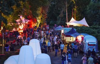 Ansicht des Localize Festivalgeländes in der Natur am Abend, mit bunter Beleuchtung und vielen Besuchenden
