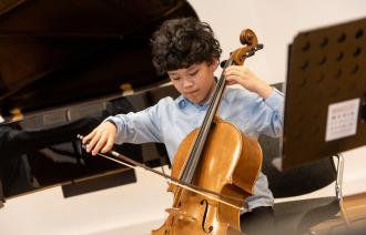 Ein sehr junger Cellist spielt engagiert sein Cello. Das Bild steht etwas schief und wirkt dadurch sehr dynamisch