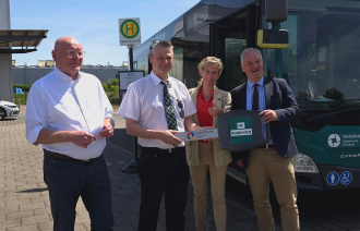 Drei Männer und eine Frau stehen seitlich von einem Bus und halten einen Schlüssel.