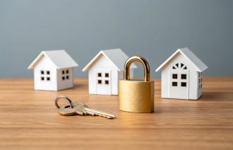 Drei kleine weiße Häuser (max. 5 cm hoch), im Vordergrund ein Schloss und ein Schlüssel.