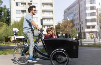 Ein Mann fährt auf einem Lastenrad mit Kindern vorne im Kasten.