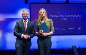 Bei der Verleihung des Nachwuchswissenschafts-Preises 2023 stehen Oberbürgermeister Mike Schubert und die Preisträgerin Dr. Lisa Schwetlick gemeinsam strahlend auf der Bühne. 