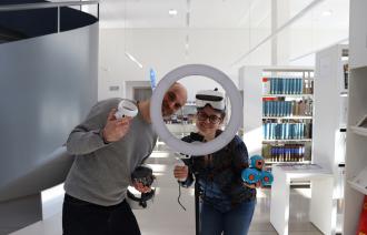 Zwei Mitarbeitende der SLB tragen VR-Brillen und schauen durch einen Beleuchtungsring.