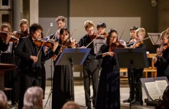 Erfahrene Musizierende an klassischen Instrumenten sind gemeinsam mit jugendlichen Talenten in Aktion zu sehen