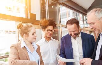 4 Personen im Büro, die freundlich lächeln und auf einem Blatt Papier schauen