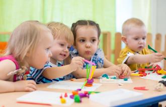 Vier Kita-Kinder sitzen an einem Tisch und basteln mit bunter Knete.