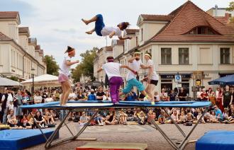 Menschen springen auf einem Trampolin in der Innenstadt, darum sammelt sich eine Gruppe Zuschauende
