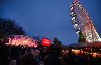 Unter blauem Nachthimmel sehen wir das beleuchtete Riesenrat und viele Menschen, die zu einer schönen Bühne strömen