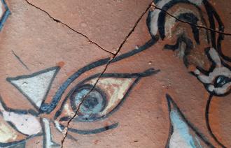 Das Foto zeigt einen Teil einer bemalten Keramik. Zu sehen sind unter anderem ein gezeichnetes Auge und ein Ohr.