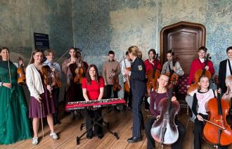 viele Jugendlich mit Musikinstrumenten sitzen mit ihren Instrumenten in einem historischen Schlossambiente