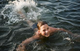 Eine Junge schwimmt in einem See und schaut lächelnd in die Kamera..