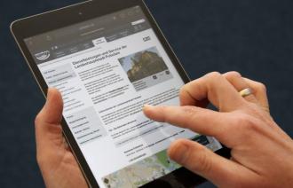 Das Foto zeigt ein Tablet mit einer Unterseite von potsdam.de und eine Hand, die darauf navigiert.