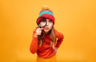 Ein Kind blickt durch eine Lupe in die Kamera. 