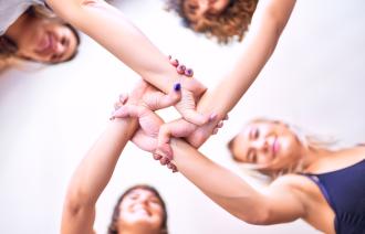 Vier Frauen halten sich an den Handgelenken und bilden damit einen Kreis.