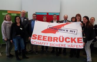 Teilnehmende des Arbeitstreffens im April halten zusammen mit OBM Mike Schubert ein Transparent mit dem Aufdruck: Solidarisch mit Seebrücke.
