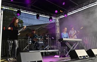 Ein Jazzquartett spielt auf einer Open-Air-Bühne. Magentafarbenes Scheinwerferlicht und etwas künstlicher Rauch sorgt für Stimmung.
