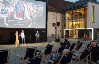 Mehrere Menschen sitzen in Liegestühlen und wohnen einem Open-Air Kino bei.