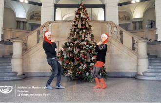 Ein Sänger und eine Sängerin posieren im Weihnachtslook vor einem Weihnachtsbaum