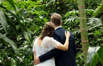 Auf dem Foto ist ein sich umarmendes Hochzeitspaar in der Tropenwelt der Biosphäre zu sehen.