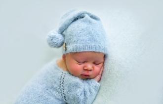 Das Foto zeigt ein schlafendes Baby in blauem Strampelanzug mit blauer Zipfelmütze.