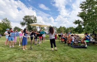 ein kleines Kinderstreichorchester probt auf einer Wiese bei schönstem Sommerwetter