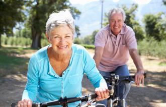 Das Foto zeigt im Vordergrund eine Seniorin und dahinter einen Senior auf dem Fahrrad.