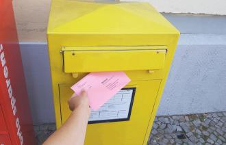 Eine Hand steckt einen Wahlbrief in einen Briefkasten.