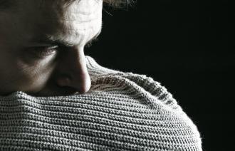 Das Schwarz-Weiß-Foto zeigt als Beispiel für eine traurige, depresive Stimmung einen jungen Mann, der seinen Kopf in die Armbeuge seines Pullovers drückt und selbstverloren in sich und in die Welt schaut.