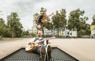 Mann mit Gitarre auf einem Trampolin, dahinter springt ein Mensch, Foto: der bunte hund, Lizenz: der bunte hund
