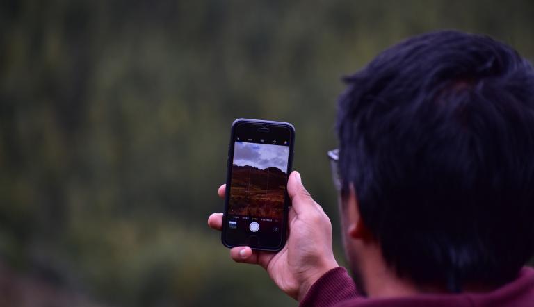 Ein Mann geht mit einem Mobiltelefon in der Hand durch die Natur.