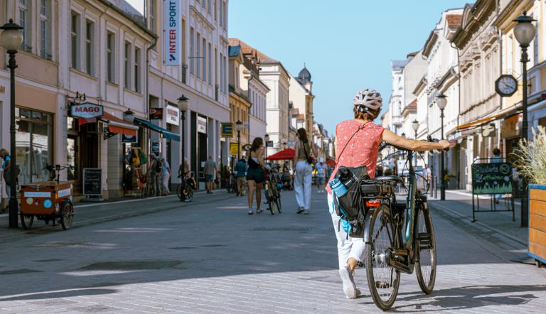 Eine Radfahrerin, die ihr Fahrrad durch die Brandenburger Straße schiebt.