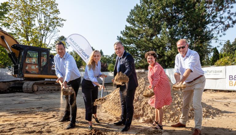 Fünf Personen setzen den Spatenstich auf einer Baustelle