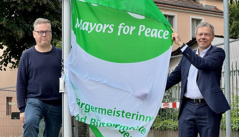 Bürgermeister Burkhard Exner und Uwe Fröhlich vom Hiroshima-Platz-Verein mit der Flagge Mayors for Peace.