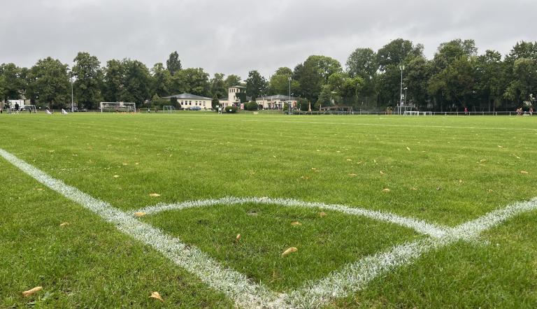 Die weißen Seitenlinien einer Ecke des Sportplatzes an der Berliner Straße sind zu sehen, im Hintergrund des Fußballplatzes steht das einstöckige Vereinsgebäude