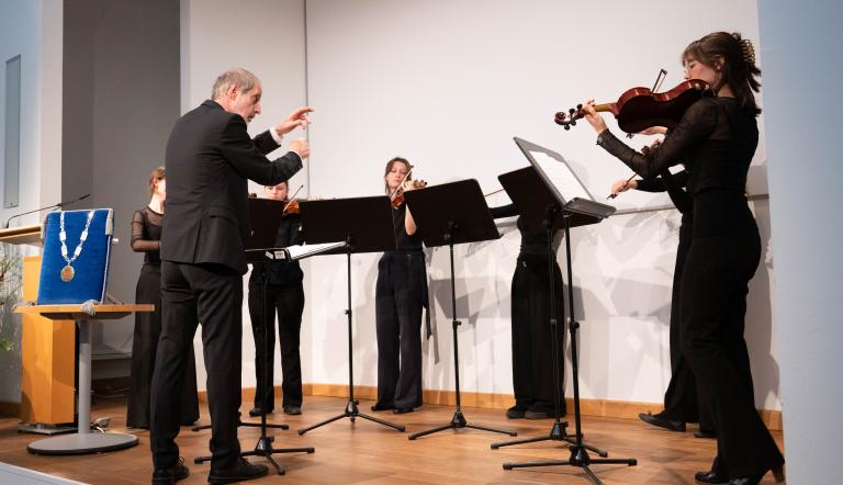 Schülerinnen der Musikschule werden dirigiert und spielen auf ihren Geigen.