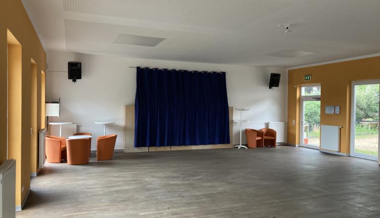 Das Foto zeigt den leeren und aufgeräumten Saal im Bürgerhaus "Kirchbergtreff" Neu Fahrland mit einigen Einrichtungsgegenständen wie Sessel und Stehtischen.
