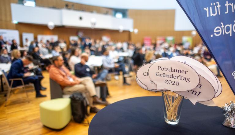 Sprechblasen auf einem Stehtisch vor verschwommenem Publikum